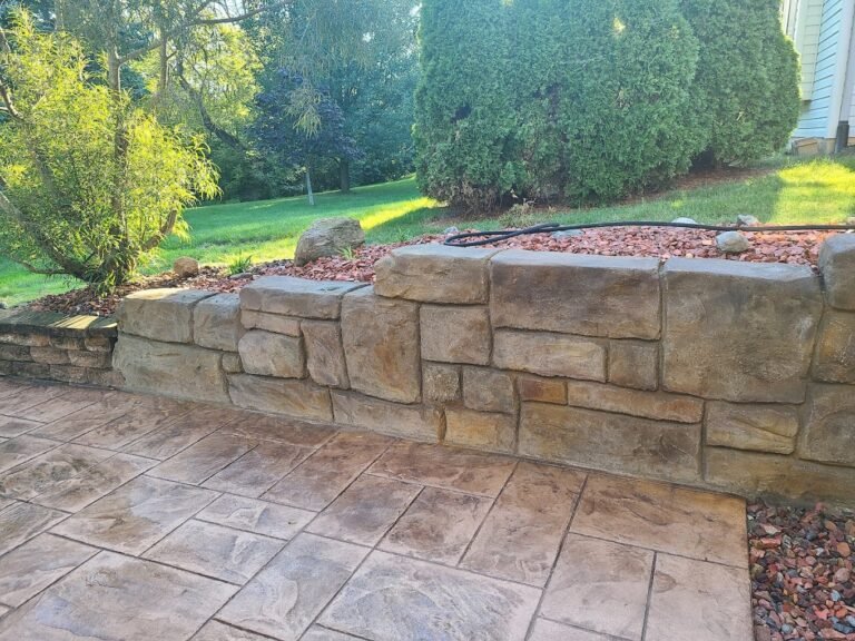 Stone look retaining walls on the side of a patio. Green trees in the background Concrete Contractor in Bryan, OH