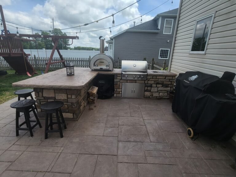 Island on a patio that has a BBQ, pizza oven, and chairs