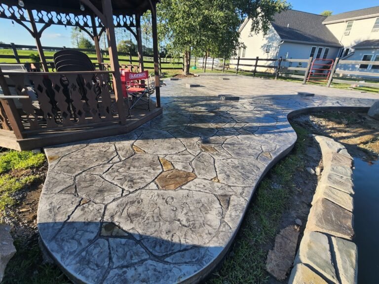 Low shot of a stamped patio with a Gazebo to the left, and a white house in the background.