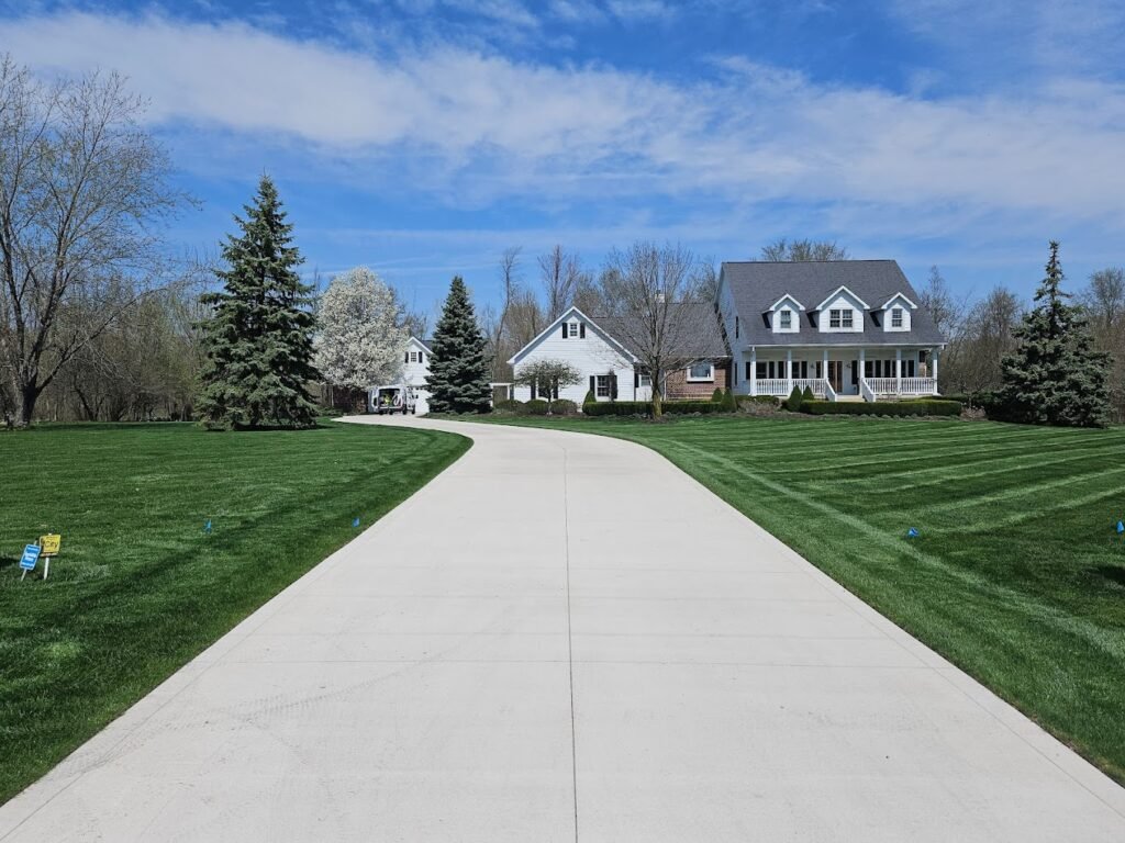 Long driveway surrounded by grass with a home in the background. Driveway replacement in Churubusco