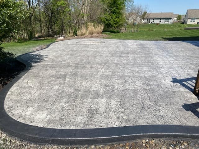 Concrete patio with a smooth black border in a spacious backyard, offering a modern and durable outdoor living space.