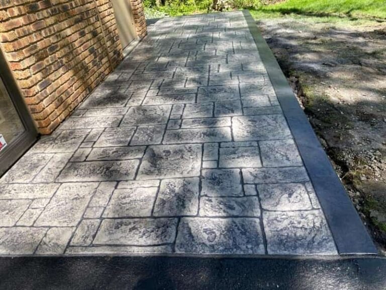 Stamped concrete patio with an English Ashlar stone pattern and a dark border, installed beside a brick home.