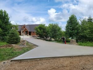 Freshly poured concrete driveway leading to a custom-built home surrounded by trees, showcasing the work of Fort Wayne concrete contractors.