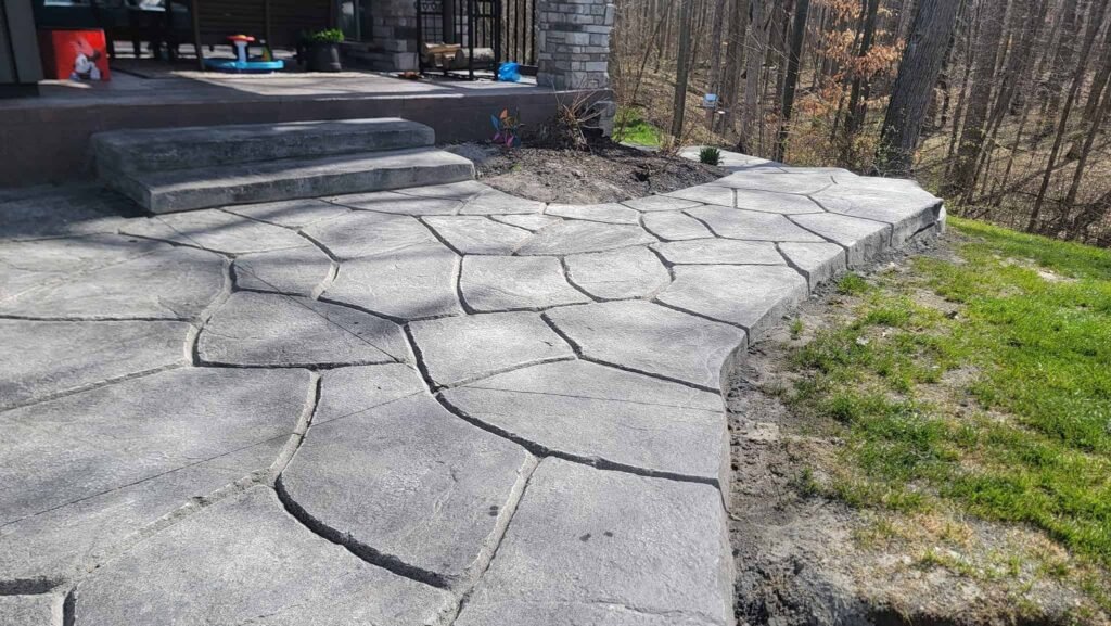 Stamped concrete patio with a natural stone design in a backyard near a wooded area. Showing off Stamped Concrete in Fort Wayne. Stamped concrete in Auburn